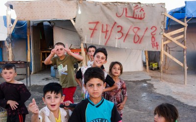 Behind the children a very representative banner for the yazidi community: it recalls how many times they were persecuted in the history of humanity - 74 times in total in several wars - and the last persecution, made by Islamic State (ISIS). Sharia Refugee Camp, near Duhok, Iraq (Iraqi Kurdistan).