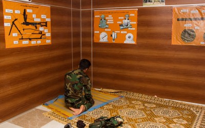 Peshmerga in religious time. Some bases share the space for daily prayers with posters explaining to soldiers about armaments and combat strategies. Iraq (Iraqi Kurdistan), Middle East, 2015.